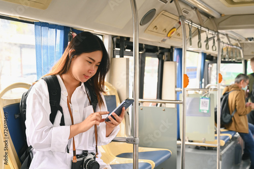 Smiling young woman passenger using mobile phone while traveling by bus. Public transportation concept.