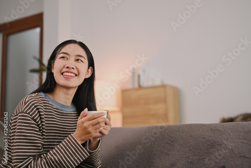 Bild auf Leinwand Beautiful young woman holding coffee cup and looking away, enjoying morning coff