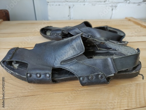 Shabby black men's leather sandals on the wooden background