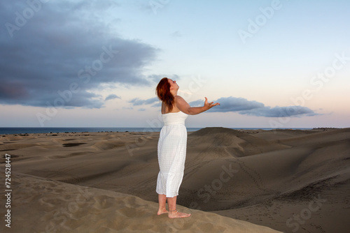 Young woman stands in the sand dunes with theatrical hand gesture