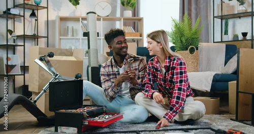 Couple man and woman having fun together when guy fooling around with pliers during assembling chair in their new flat photo