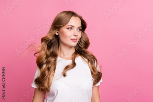 Photo of gorgeous woman with wavy fluttering hairstyle dressed stylish t-shirt look at promo empty space isolated on pink color background © deagreez