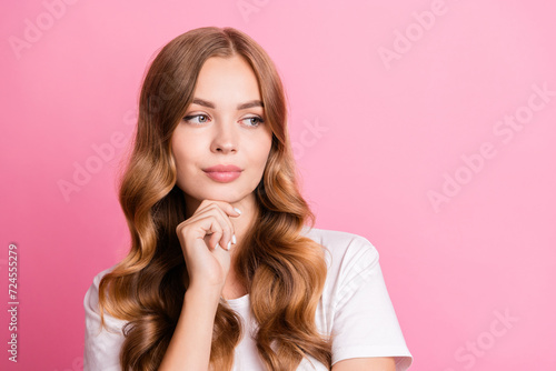 Photo of lovely pensive woman with wavy hairstyle dressed white t-shirt hand on chin look empty space isolated on pink color background