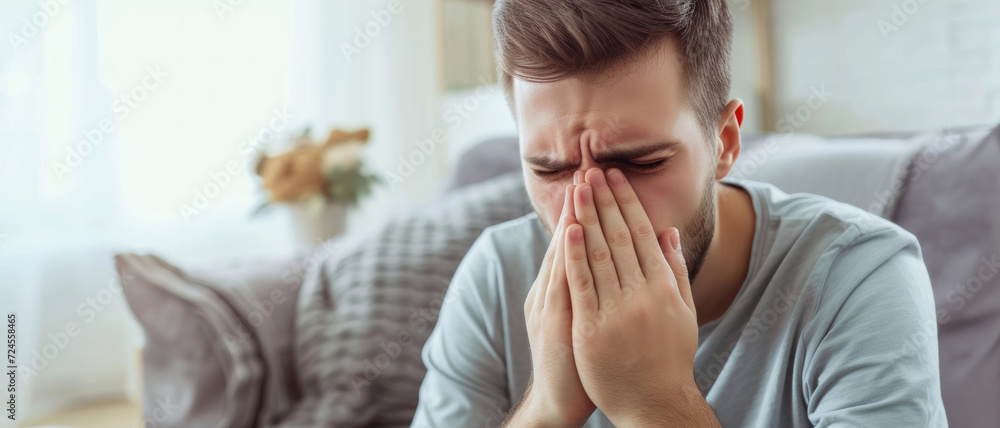A distressed man covers his face with hands, a powerful display of despair or headache in a serene home setting A distressed man covers his face with hands, a powerful display of despair or headache in a serene home setting