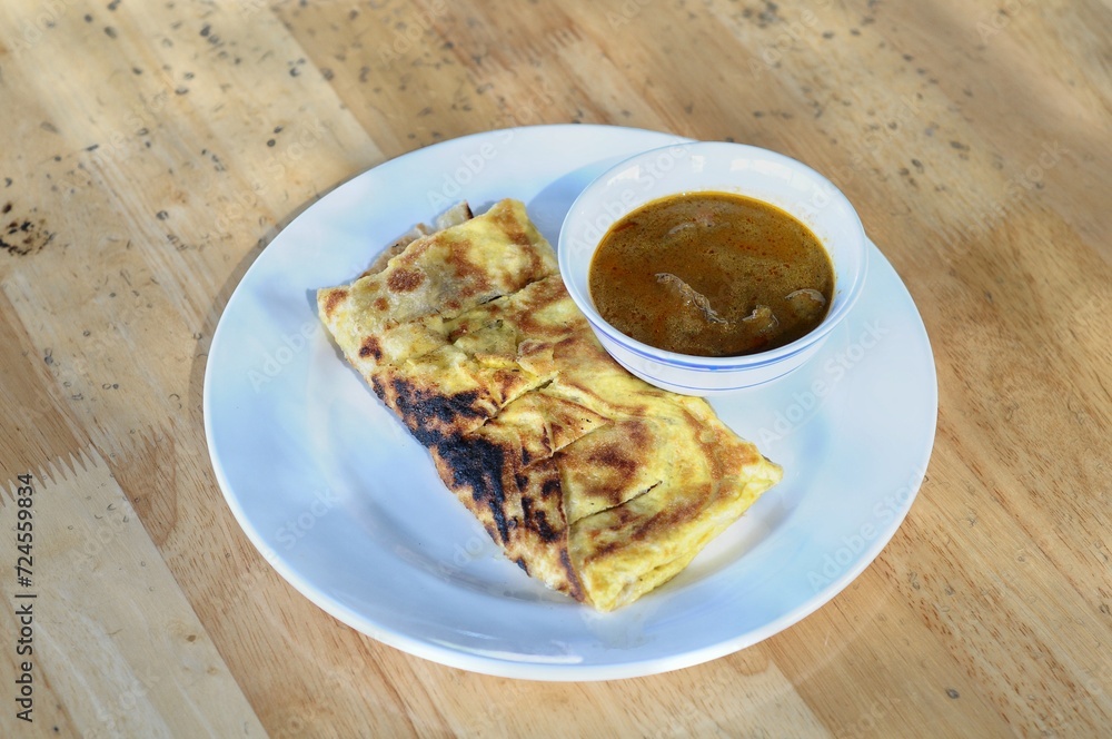 roti canai with chicken curry served on a white plate and wooden table