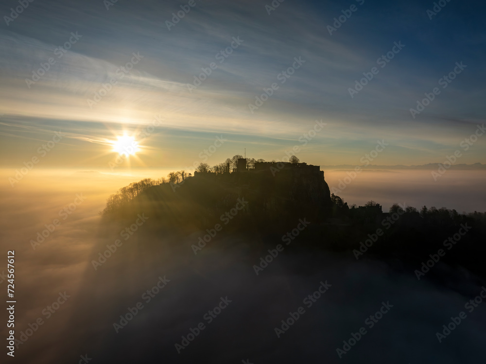 Fototapeta premium Luftbild vom Hegauvulkan Hohentwiel mit der oberen Festungsruine als Silhouette bei Sonnenaufgang, die bei einer Inversionswetterlage aus dem Nebel herausragt