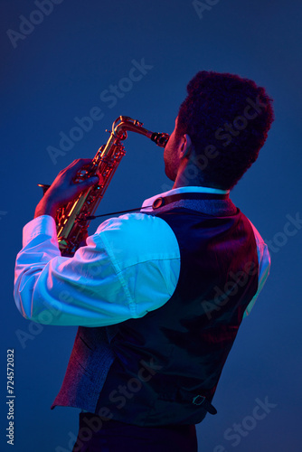 Photography Rear view of man playing sax performing jazz melodies against vibrant blue background in mixed pink-purple background