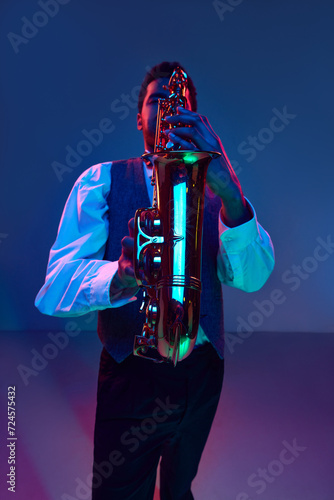 Jazzman. Elegant saxophonist dressed white shirt and vest playing jazz melodies in blue-pink light against gradient studio background. Concept of jazz, blues, classy instrumental music, festivals. Ad photo