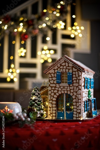 Big gingerbread house standing in the Christmas decorated room with lights, candle and Christmas tree