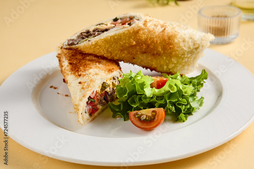 Grilled beef shawarma sandwich on a white plate, garnished with fresh lettuce and tomato. Suitable for fast food advertising and snack bar menus