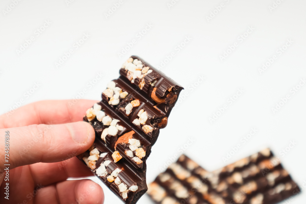 A piece of bitter dark chocolate bar with nuts in hand. Sweets addiction. Man eating a bar of chocolate