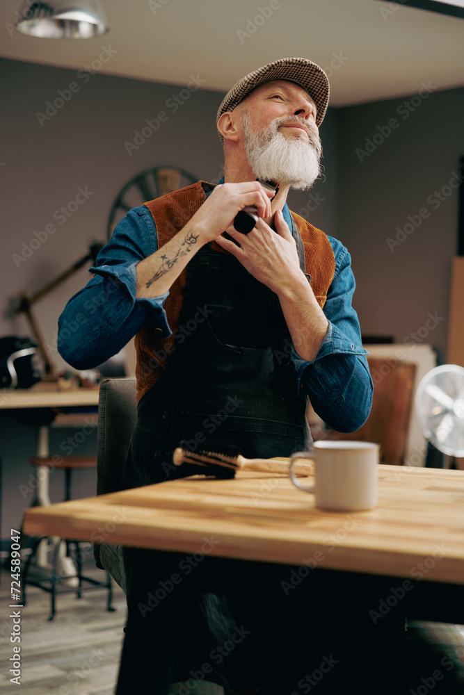 Portrait d'un hipster barbier avec une belle barbe en train de se raser avec une tondeuse dans un atelier magasin Portrait d'un hipster barbier avec une belle barbe en train de se raser avec une tondeuse dans un atelier magasin