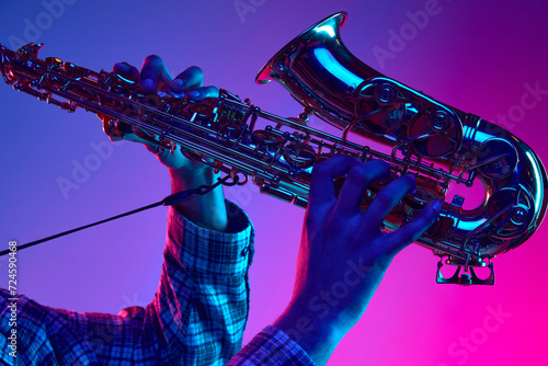 Cropped portrait of jazzman playing saxophone against gradient blue-pink background in neon light. Jazz melodies. Concept of classical musical instrument, concerts and festivals. Ad