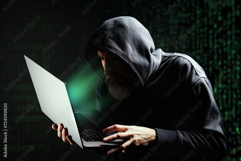 Pirate informatique masqué en train de pirater un ordinateur portable et qui demande une rançon devant un écran vert Pirate informatique masqué en train de pirater un ordinateur portable et qui demande une rançon devant un écran vert
