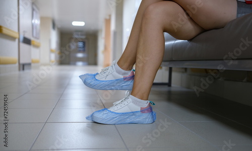 Woman in shoe covers sitting in hospital corridor closeup. Sanitary norms of behavior in medical institutions concept photo
