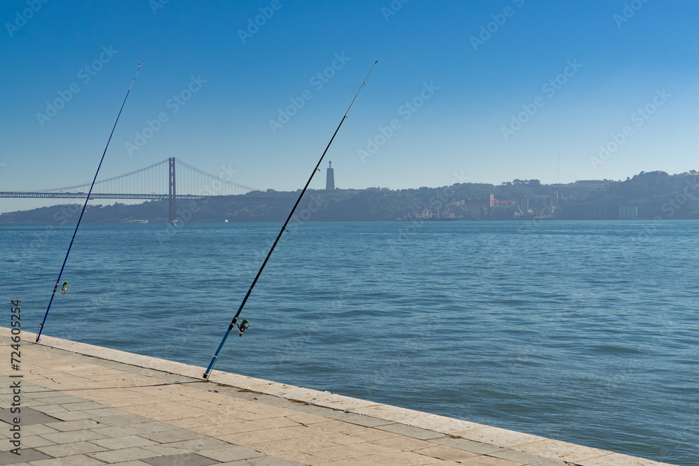Two fishing rods in Lisbon in Portugal, the bridge of the 15th April and the Cristo Rei in the background Two fishing rods in Lisbon in Portugal, the bridge of the 15th April and the Cristo Rei in the background