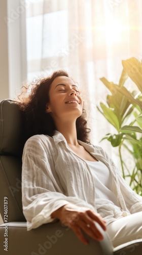 A Happy woman sitting in comfortable chair in home design, relaxing, breathing fresh air. A smiling young female tenant or a tenant relaxing in an armchair relieves negative emotions