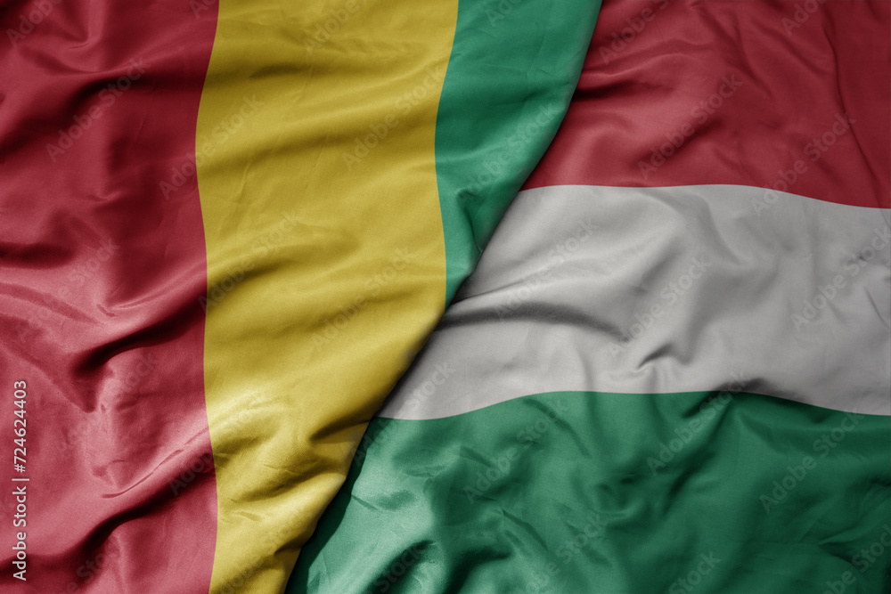big waving national colorful flag of hungary and national flag of guinea .