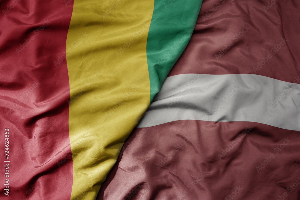 big waving national colorful flag of latvia and national flag of guinea .