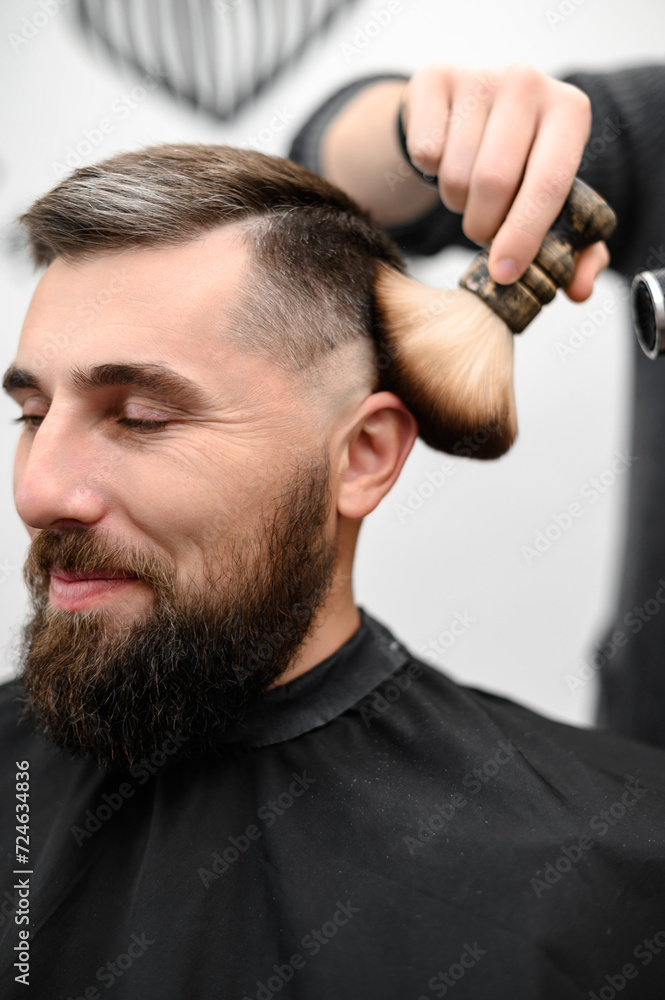 Fototapeta premium Barber sweeps hair with a brush while cutting a client hair in a salon.