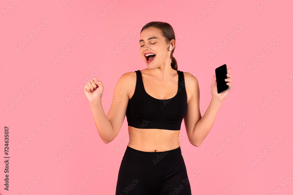 Energetic young woman in sportswear dancing and enjoying music from her smartphone Energetic young woman in sportswear dancing and enjoying music from her smartphone
