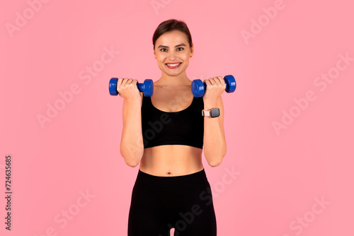 Smiling sporty woman doing fitness routine  training with blue dumbbells