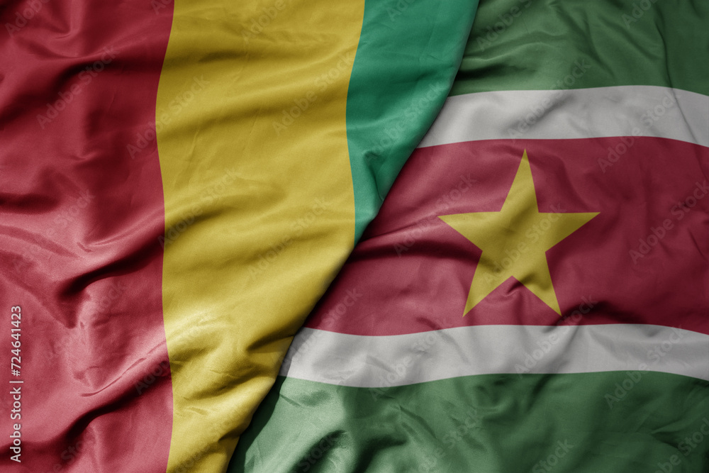 big waving national colorful flag of suriname and national flag of guinea .