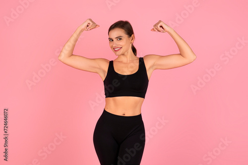 Confident and smiling fitness woman in sportswear flexing her biceps, demonstrating strength