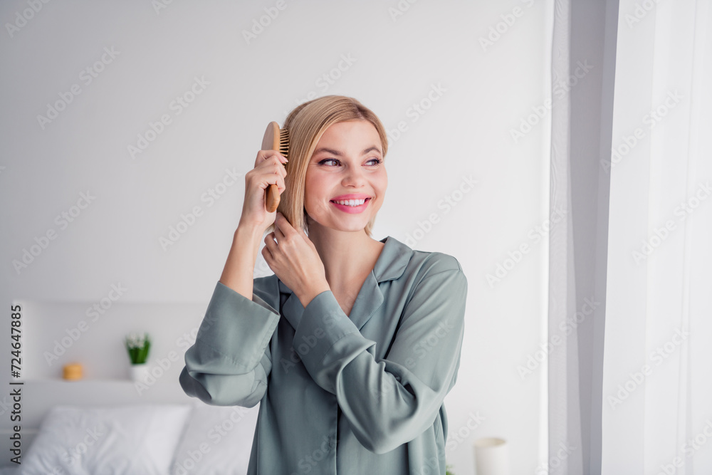 Portrait of shiny young lady wearing grey comfortable pajama during bedtime preparing to sleep brushing hair looking in window indoors Portrait of shiny young lady wearing grey comfortable pajama during bedtime preparing to sleep brushing hair looking in window indoors