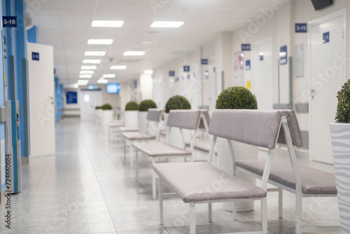 Empty modern hospital corridor, clinic hallway interior background with white chairs for patients waiting for doctor visit. Contemporary waiting room in medical office. Healthcare services concept.