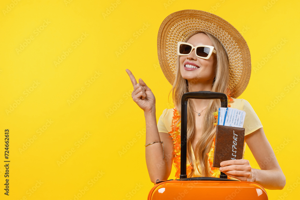 Young smiling woman pointing in vacation with suitcase and passport over isolated yellow background. Traveler on trip voyage tourist showing copy space - obrazy, fototapety, plakaty 