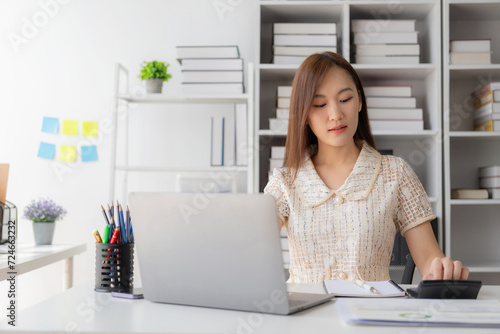 Young Asian woman sits at a table and calculates financial graphs showing investment results. Plan your business growth process with financial review and budgeting using a calculator and laptop.