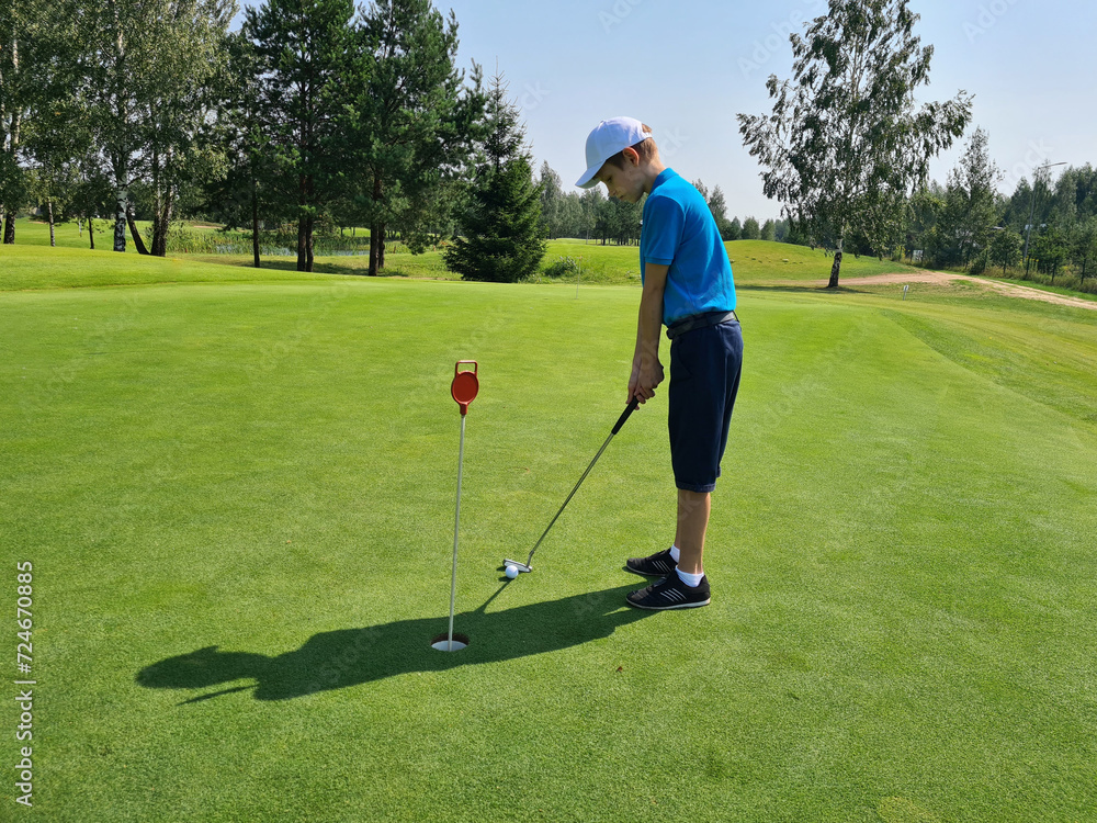 Fototapeta premium Boy plays golf on the putting green and hits ball into hole