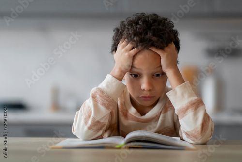 Stressed Little Black Boy Reading Book At Home And Touching Head