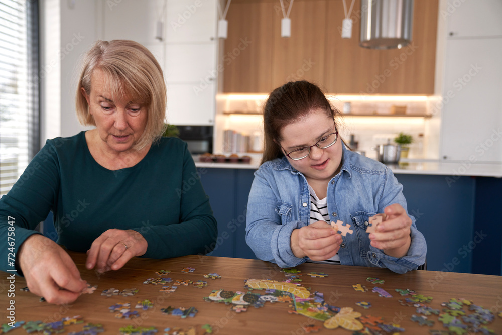 Fototapeta premium Focus down syndrome woman and her mother assembling puzzles at home