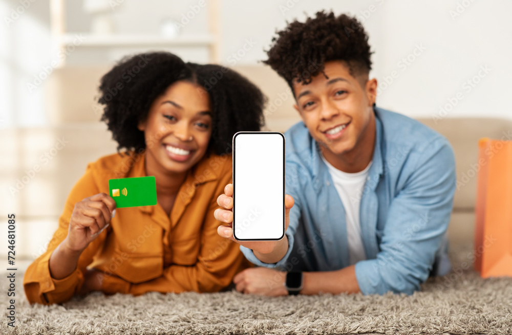 A smiling young couple on the floor shows off a smartphone and a credit card