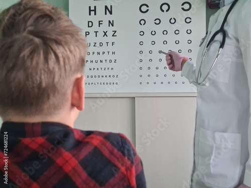 Ophthalmologist holds pen to check vision of teenage boy child photo