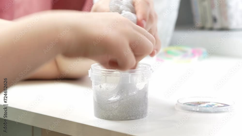 The child takes out with his hands a transparent stretching slime with silver sequins from a plastic jar. Close-up, impersonal. The child takes out with his hands a transparent stretching slime with silver sequins from a plastic jar. Close-up, impersonal.