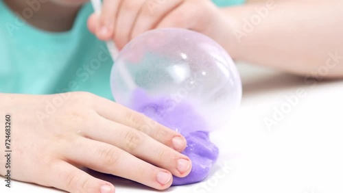 A child plays with a toy made of bright purple slime, inflates bubbles with a tube, a fashionable liquid toy sticks to his hands and fingers.