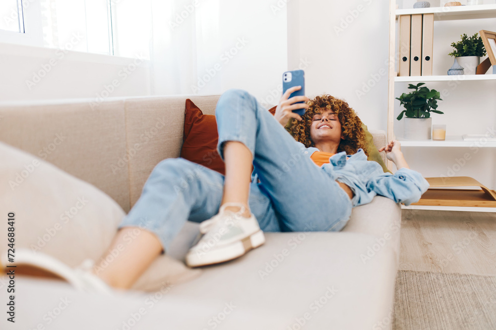 Happy woman sitting on a cozy couch at home, holding a smartphone and smiling while playing games online, reading, and chatting, creating a cheerful and engaging cyberspace. Happy woman sitting on a cozy couch at home, holding a smartphone and smiling while playing games online, reading, and chatting, creating a cheerful and engaging cyberspace.