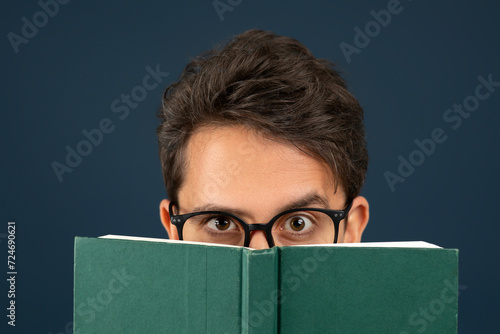 Young man wearing eyeglasses peeking over the top of green book photo