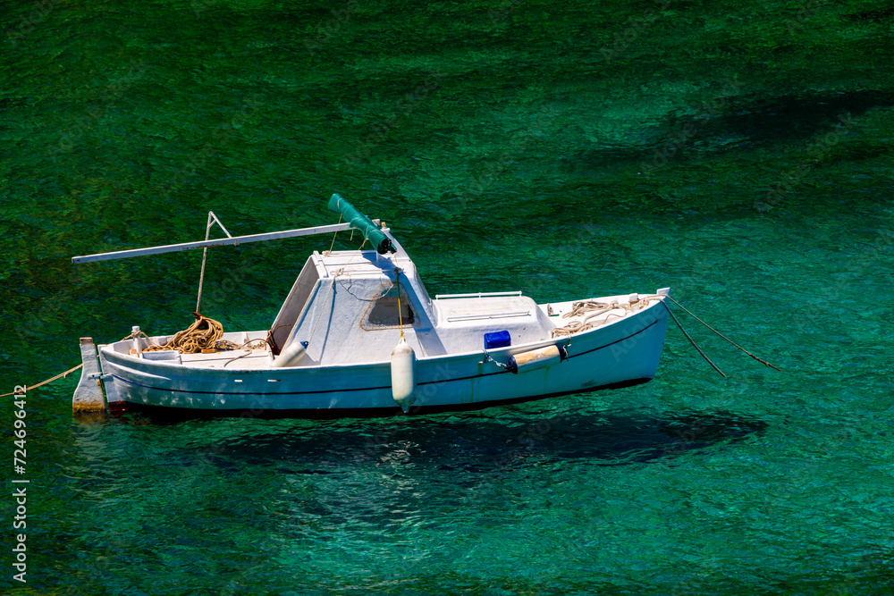 Small white fishing boat in a Croatian bay with bright turquoise water. Old wooden boat in bright sunshine anchored on Bisevo island in the Adriatic Sea. Idyllic and calm atmosphere at holiday spot.
