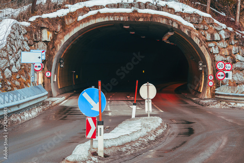 The view of the entrance to a tunnel on a highway in the Alps on a winter's day, decorated with road signs, exudes an atmosphere of mystery and exploration. Travel, transition or path concept