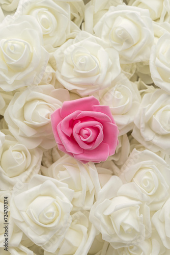 vertical image top view of background of white flowers and one pink flower. artificial flowers. Artificial white roses and one pink rose from foamiran. soft focus. flat lay
