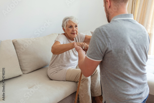Foto Female home carer supporting old woman to stand up from the sofa at car
