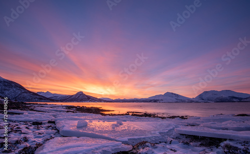 Stunning twilight sky over a snow-covered landscape near Tromsø, Norway, with icy waters in the foreground.
