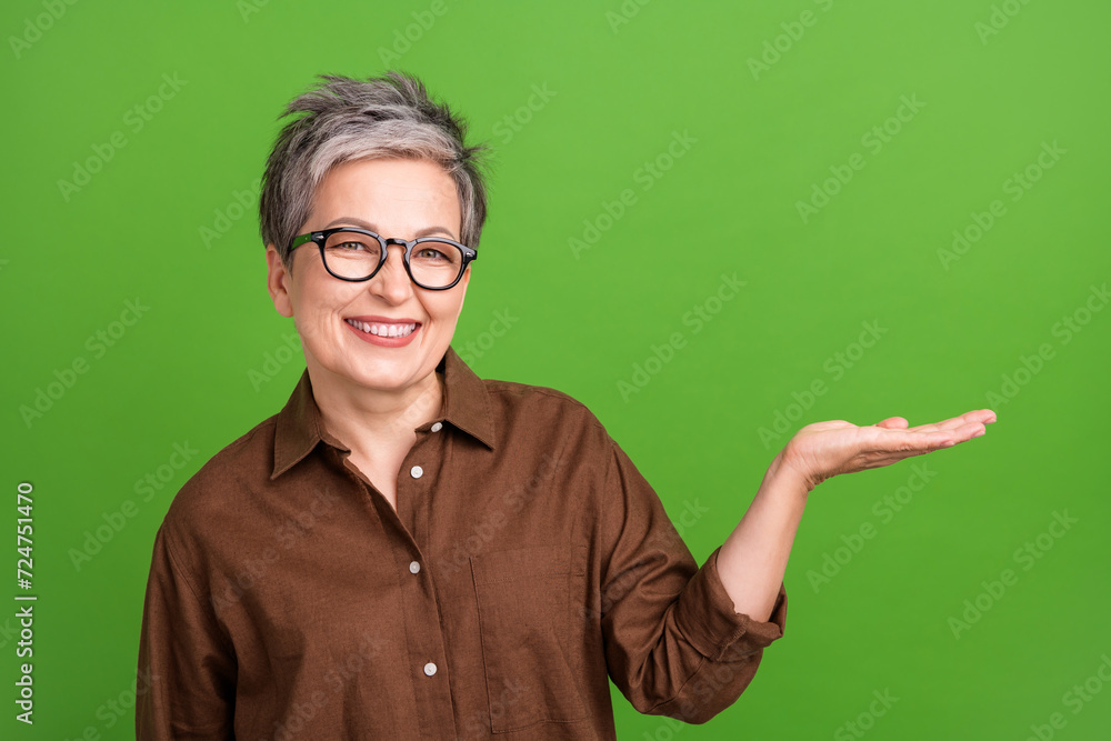 Photo of optimistic woman with short hairstyle wear brown shirt palm demonstrate object empty space isolated on green color background Photo of optimistic woman with short hairstyle wear brown shirt palm demonstrate object empty space isolated on green color background