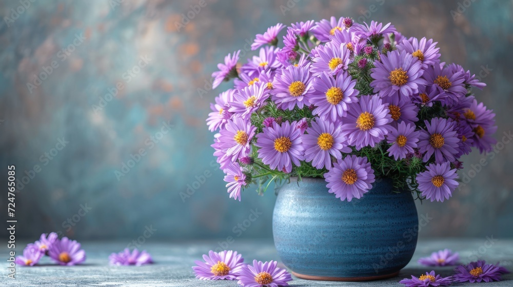 a blue vase filled with purple flowers sitting on top of a wooden table next to other purple and yellow flowers on a gray and blue tablecloth covered tablecloth. a blue vase filled with purple flowers sitting on top of a wooden table next to other purple and yellow flowers on a gray and blue tablecloth covered tablecloth.