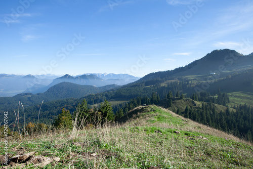 A lush green hill dotted with trees, framed by majestic mountains in the distance.