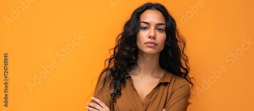 A confident Latin woman plotting deviously against an orange wall.